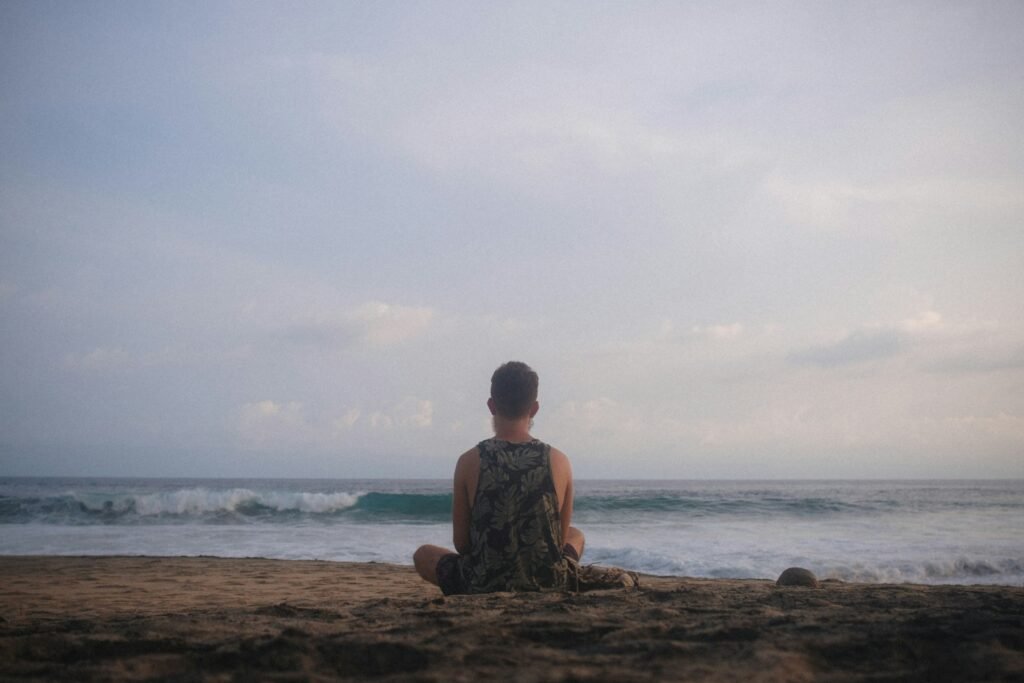 man in brown and black camouflage shirt sitting on brown rock near body of water during